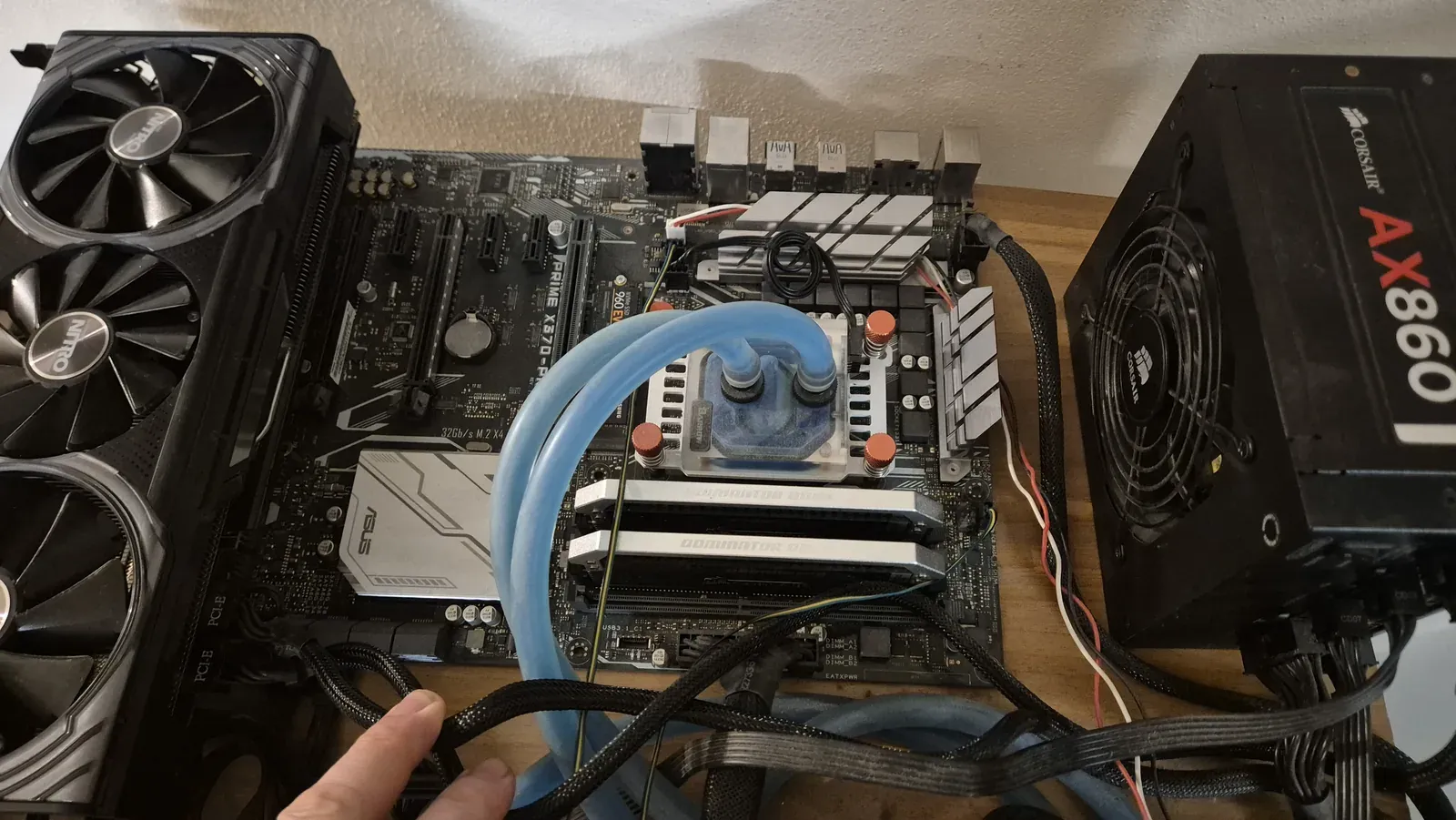 Scheda madre e scheda video montate sul banco, con due tubi azzurri sul blocco della CPU e l’alimentatore a lato