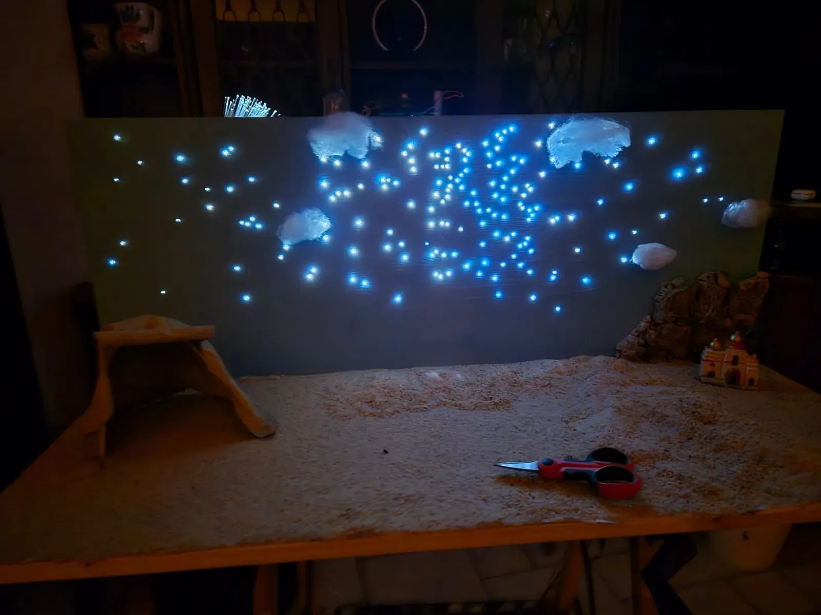 Il presepe al buio: il cielo di fibre ottiche acceso sopra la sabbia, con nuvole di ovatta, la tenda e un palazzo tra le rocce