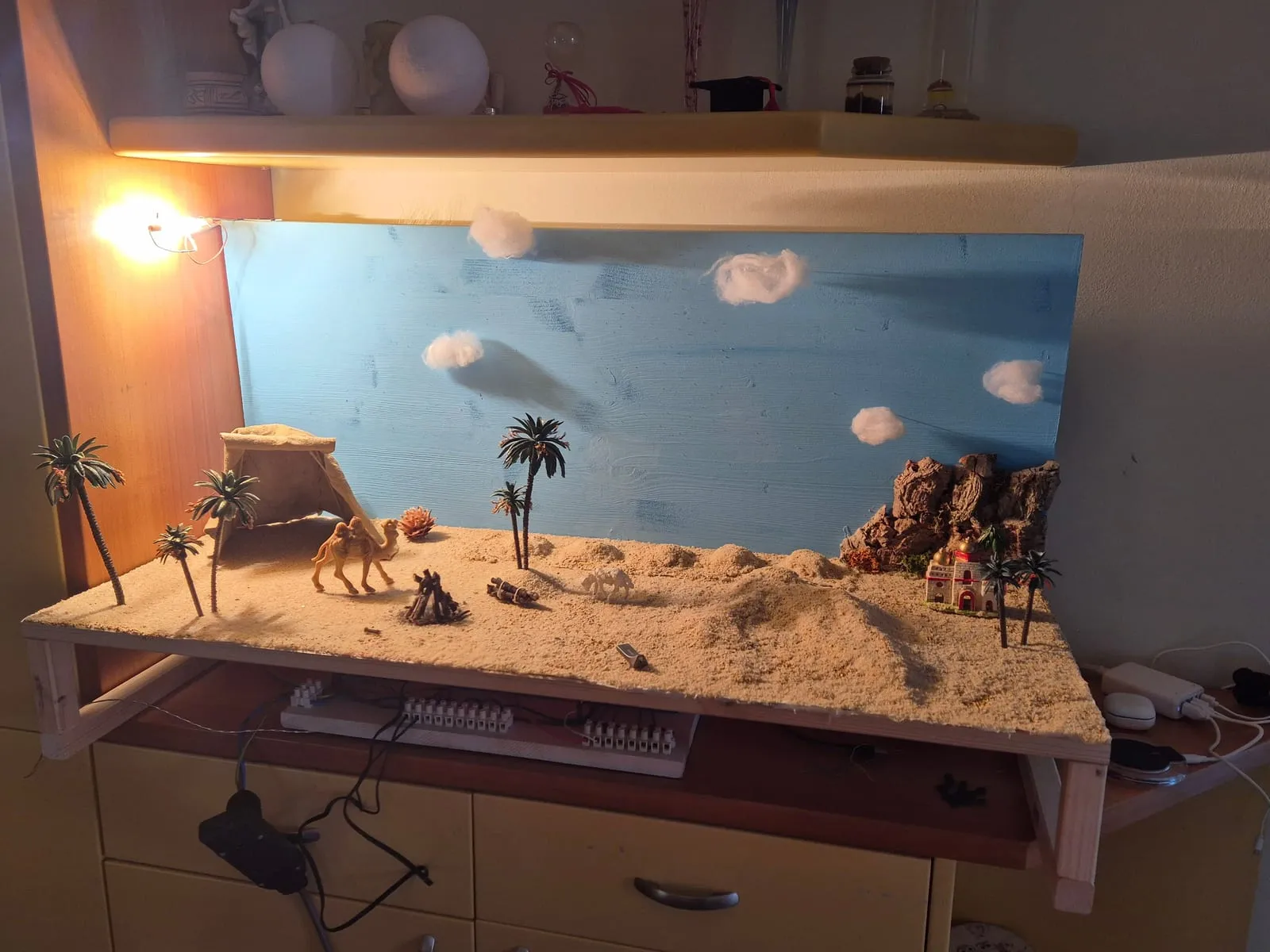 Il diorama illuminato da una lampada calda: sabbia, palme, tenda, cammello e un palazzo tra le rocce