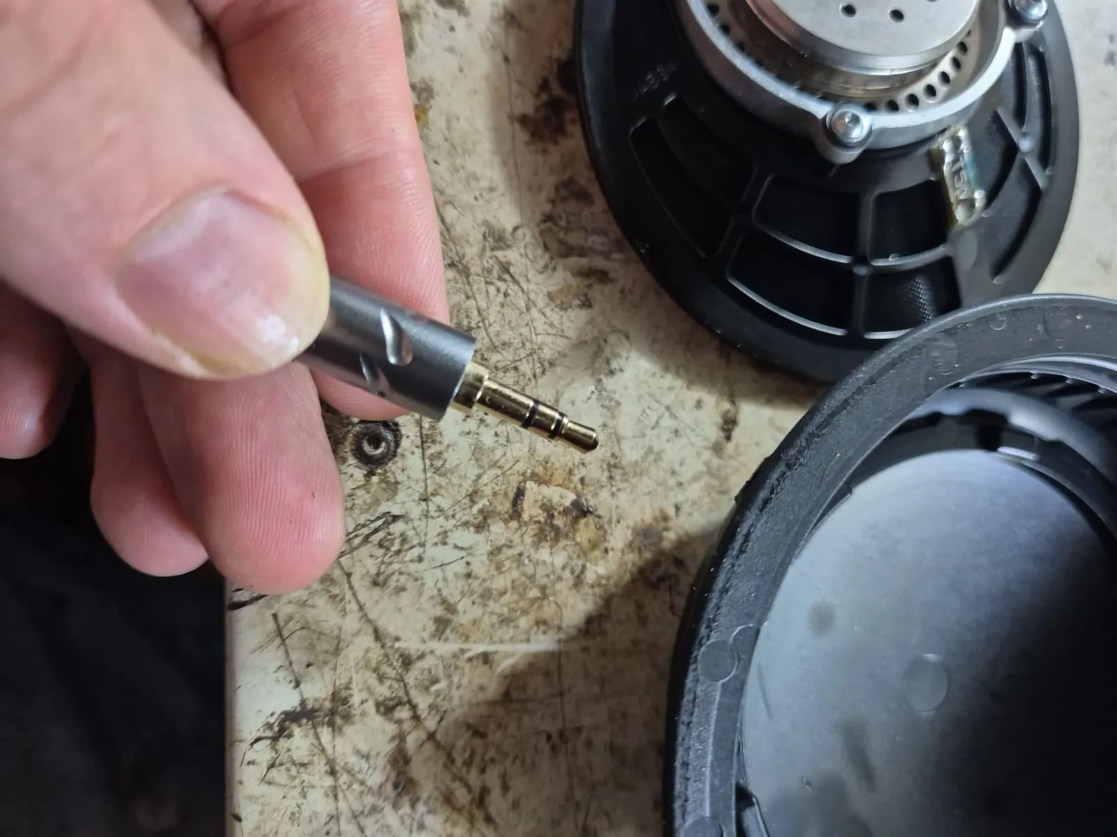 Un jack da 3,5 mm tenuto tra le dita, accanto ai padiglioni smontati