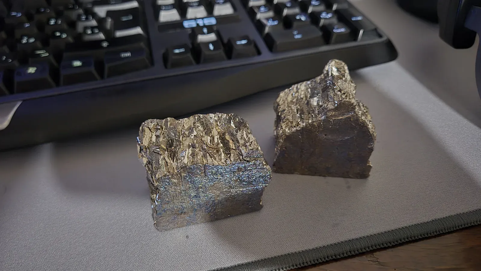 Due pezzi di bismuto dalle superfici irregolari e metalliche, appoggiati davanti a una tastiera