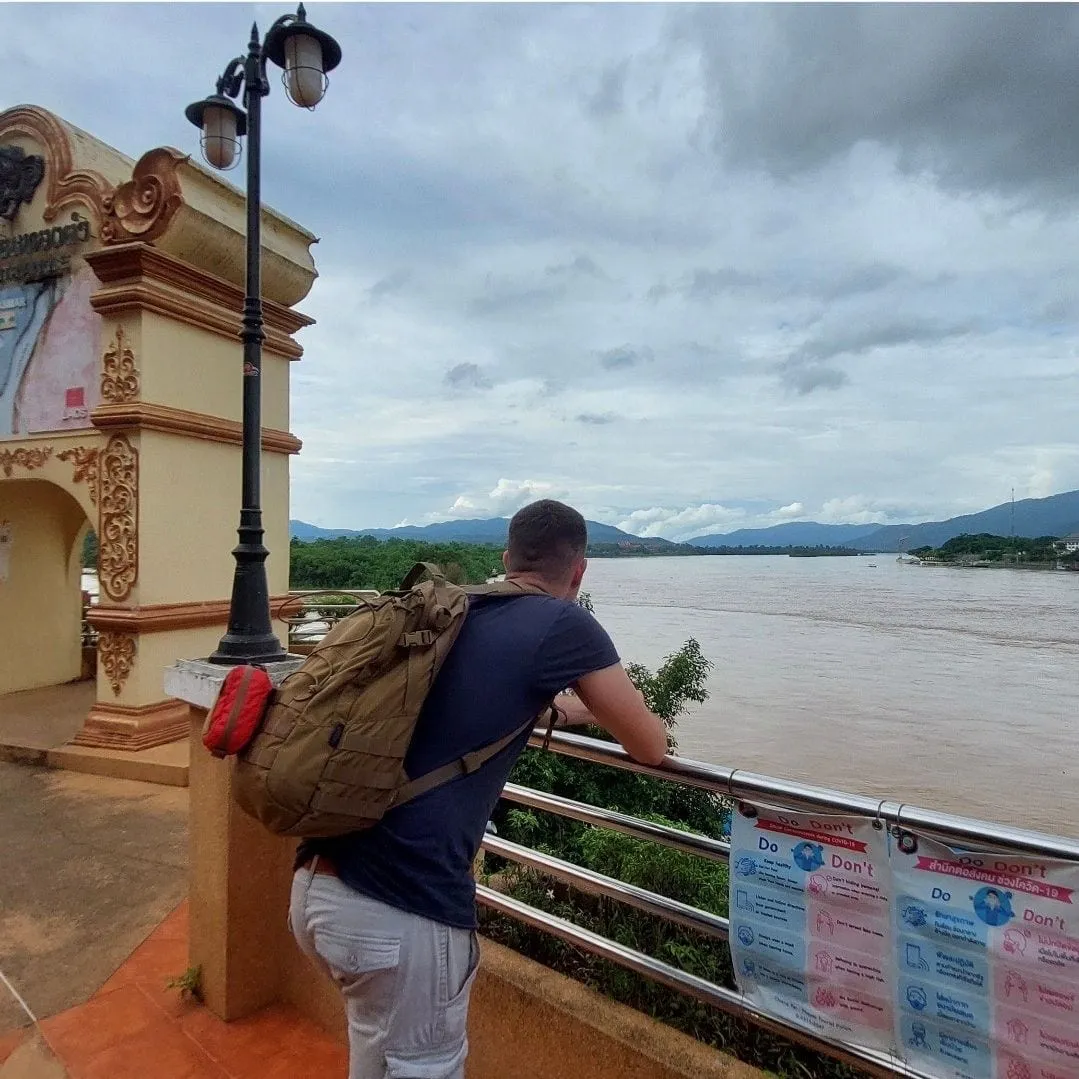 Gabriele di spalle, appoggiato alla ringhiera davanti al Mekong, sotto un cielo nuvoloso